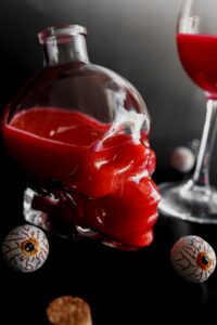 Glass skull filled with red colored wine next to wine glass